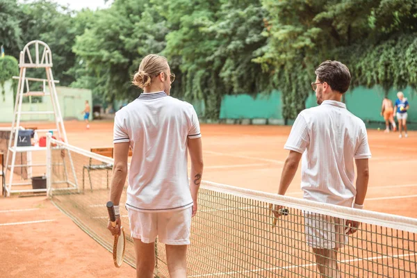 Спортивні тенісисти в білому спортивному одязі з дерев'яними стійками, що ходять біля мережі на корті — стокове фото