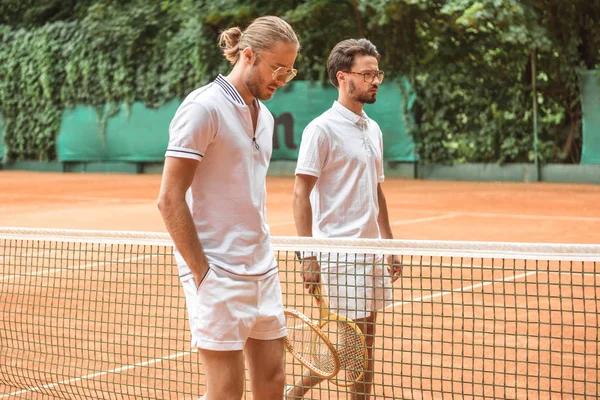 Tennis players in white sportswear with wooden rackets walking near net on court — Stock Photo
