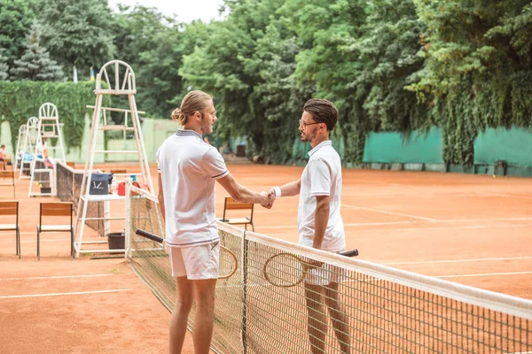 Joueurs de tennis masculins avec des raquettes en bois serrant la main après le match sur le terrain — Photo de stock