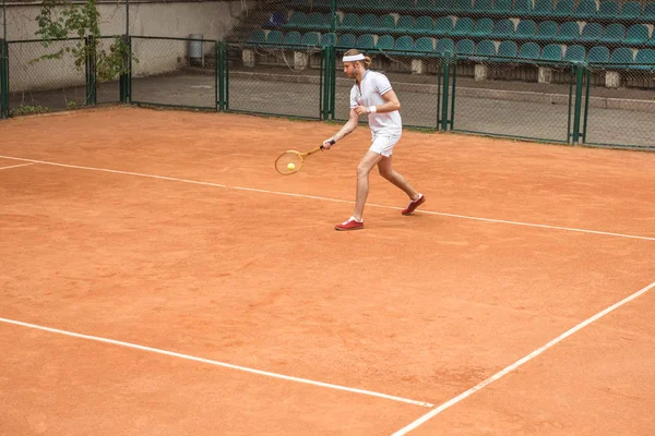 Homme de style rétro en vêtements de sport blanc jouant au tennis avec raquette et balle sur le court — Photo de stock