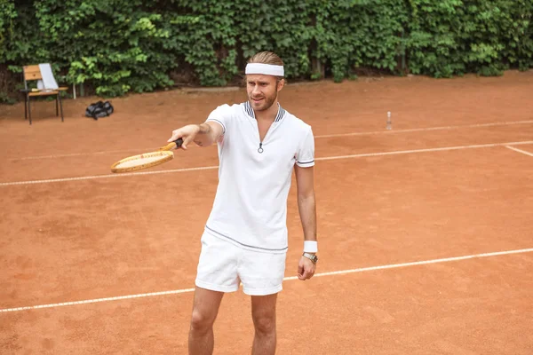 Guapo tenista apuntando con raqueta en la cancha - foto de stock