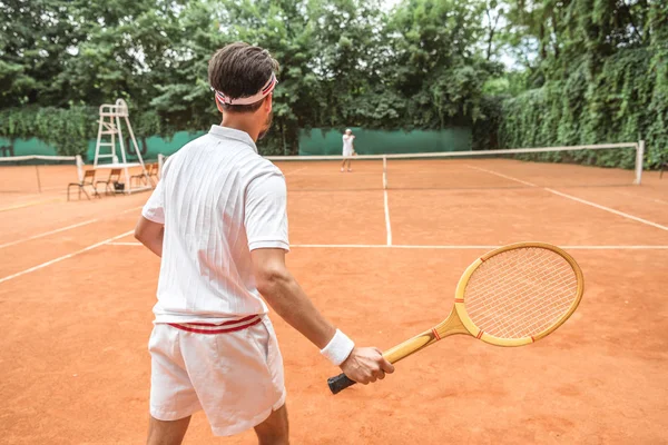 Visão traseira do desportista jogar tênis com raquete de madeira no campo de ténis — Fotografia de Stock