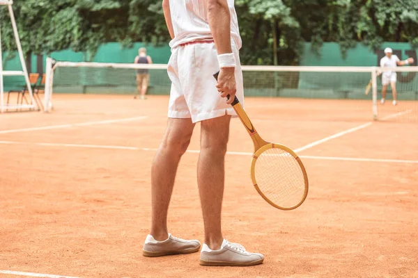 Обрізаний вид тенісиста, який тримає ретро дерев'яну ракетку і стоїть на тенісному корті — стокове фото