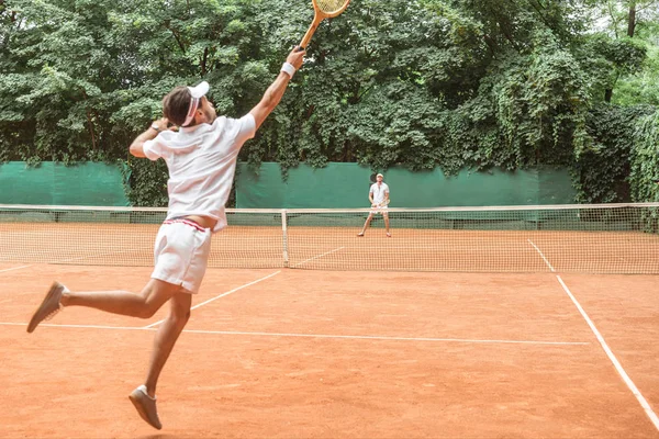 Sportsman jumping while playing tennis with friend on court — Stock Photo