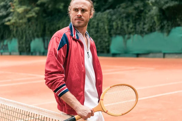 Schöner Mann mit hölzernem Tennisschläger steht am Netz auf dem Tennisplatz — Stockfoto