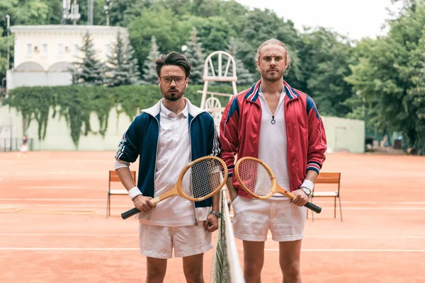 Old-fashioned friends with wooden rackets posing on tennis court with net — Stock Photo