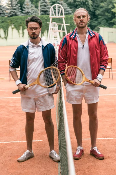 Amigos estilo retro com raquetes de madeira posando na quadra de tênis com rede — Fotografia de Stock