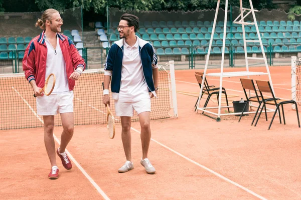 Athletic friends with wooden rackets walking on tennis court — Stock Photo