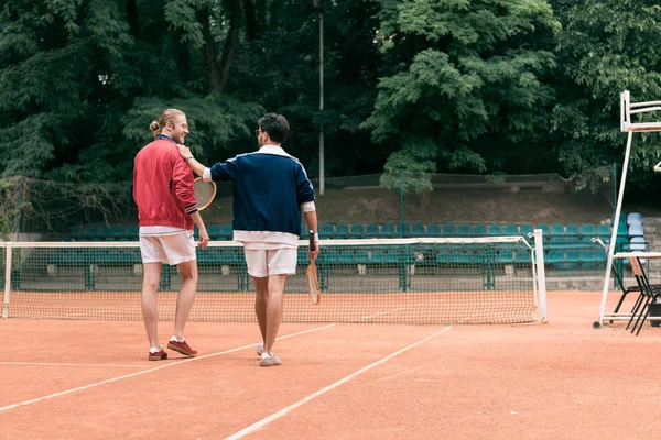 Rear view of old-fashioned friends with wooden rackets walking on tennis court — Stock Photo