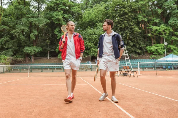 Retro styled friends with wooden rackets walking on tennis court — Stock Photo