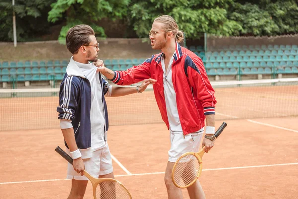 Angry sportsmen with wooden rackets conflicting on tennis court — Stock Photo
