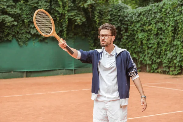 Schöner Tennisspieler zeigt mit Holzschläger auf Tennisplatz — Stockfoto