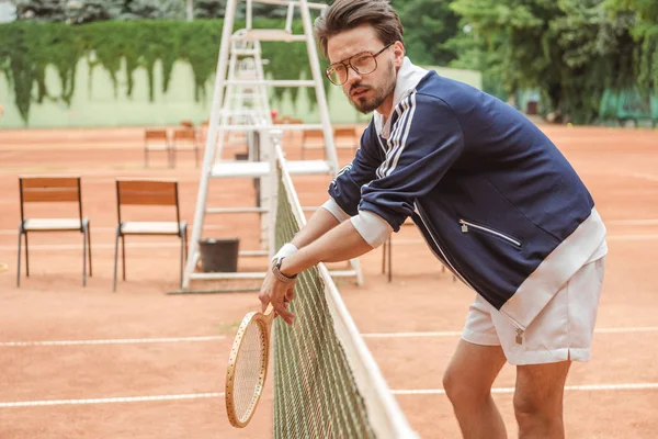 Joueur de tennis de style rétro avec raquette en bois appuyée sur le filet de tennis sur le court — Photo de stock