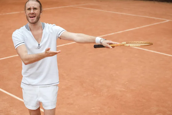 Preocupado jugador de tenis emocional que apunta con raqueta en la cancha de tenis - foto de stock