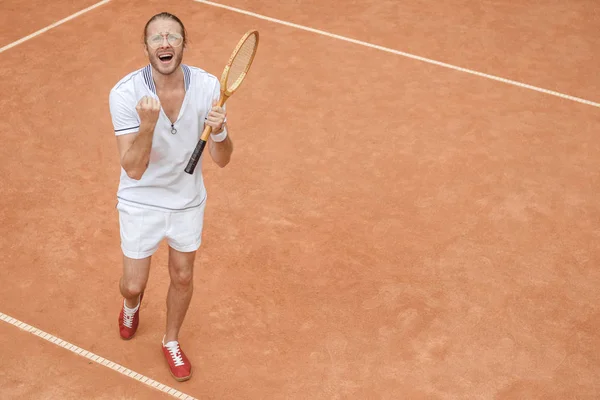 Guapo ganador emocional con raqueta gritando y celebrando en la cancha de tenis - foto de stock