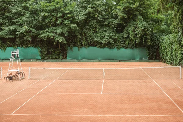 Vista de cancha de tenis marrón con sillas y red de tenis - foto de stock