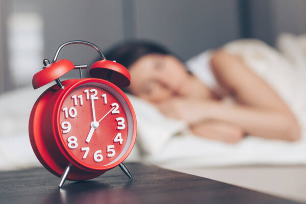 Alarm clock closeup and Young sleeping woman in bedroom at home