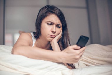 Üzgün kadın yatakta telefonda mesaj okuma