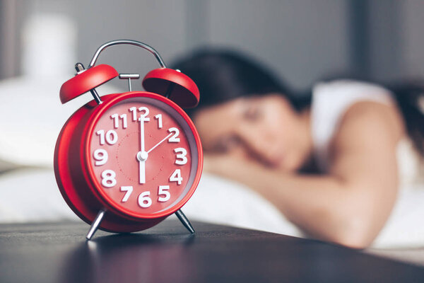 Alarm clock closeup and young sleeping woman in bedroom at home