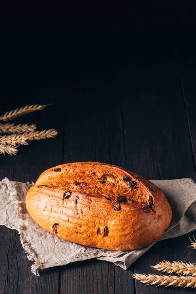 Laib braunes Brot mit Rosinen auf Textiltuch auf schwarzem Holzhintergrund mit Kopierraum — Stockfoto