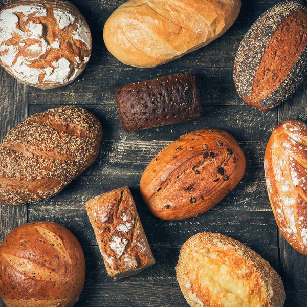 Assortiment délicieux pain fraîchement cuit sur fond en bois. Vue de dessus des pains à grains entiers noirs, bruns et blancs. Concept de boulangerie, cuisine et épicerie . — Photo