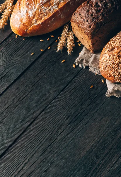 Borde de pan sobre fondo de madera negra con espacio para copiar. Diferentes tipos de pan dispuestos como un marco con espiguillas en esquina. Panadería, cocina y concepto de tienda de comestibles . — Foto de Stock