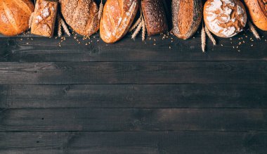 Siyah ahşap zemin üzerinde fotokopi alanı olan ekmek sınırı. Siyah, kahverengi ve beyaz, sivri uçlu tahıllı somunların bileşimi, durağan yaşam. Panorama, afiş. Fırın, aşçılık ve bakkal konsepti.