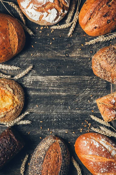 Borde de pan sobre fondo de madera con espacio para copiar. Panes integrales con espiguillas. Diferentes tipos de pan dispuestos como marco. Panadería, cocina y concepto de tienda de comestibles . — Foto de Stock