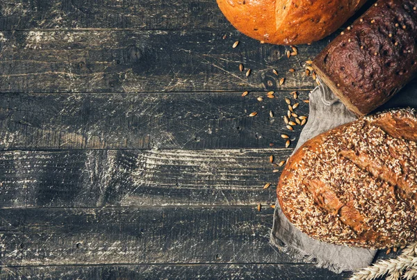 Panes marrones y blancos con espiguillas sobre fondo de madera con espacio para copiar. Tres tipos diferentes de pan. Panadería, cocina y concepto de tienda de comestibles — Foto de Stock