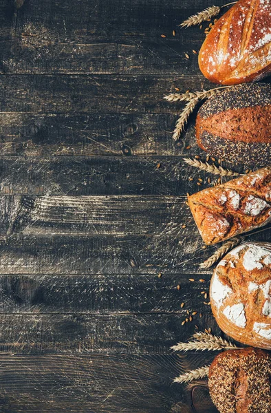 Bread border on wood background with copy space. Whole grain loaves with spikelets. Different types of bread. Bakery, cooking and grocery store concept.