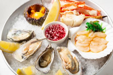 Buzlu taze deniz ürünleriyle dolu büyük bir tabak. İstiridye, kirpi, istiridye ve yengeç. Limon dilimi ve soslu deniz ürünleri manzarasını kapat. Restoranda ezilmiş buzlu deniz mahsulleri.