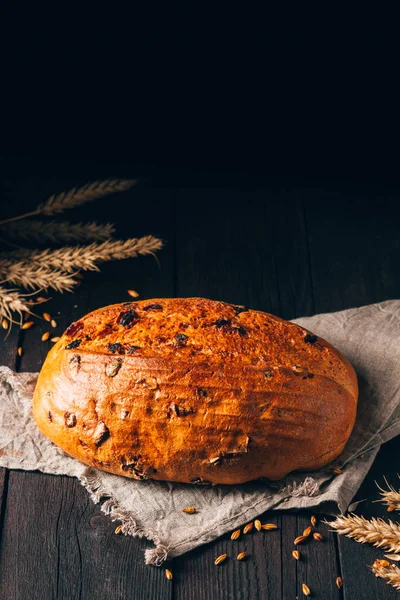 Egy vekni barna kenyér mazsolával a textil törölközőn fekete fa háttéren. Függőleges összetétel fénymásoló felülettel Stock Fotó