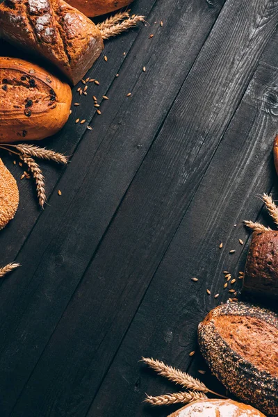 Borde de pan sobre fondo de madera con espacio para copiar. Composición vertical de panes integrales con espigas. Diferentes tipos de pan. Panadería, cocina y concepto de tienda de comestibles . —  Fotos de Stock