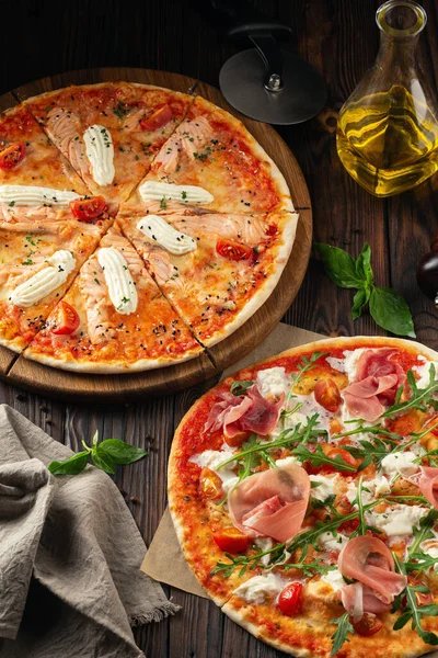 Stillleben von zwei verschiedenen Pizzen mit Messer und Flasche mit Olivenöl auf Holztisch. Cover, Speisekarte des Restaurants Stockbild