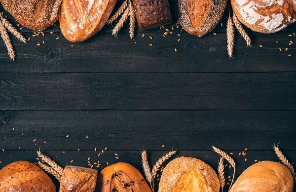 Brotrand auf Holzgrund mit Kopierfläche. Vertikale Zusammensetzung von Vollkornbroten mit Ähren. Verschiedene Brotsorten. Konzept Bäckerei, Kochen und Lebensmittelgeschäft. lizenzfreie Stockbilder