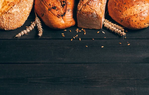 Borde de pan sobre fondo de madera oscura con espacio para copiar. Diferentes tipos de pan. Panadería, cocina y concepto de tienda de comestibles . — Foto de Stock