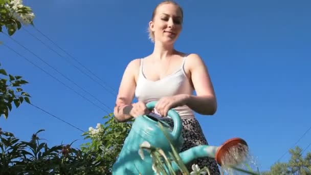Молода жінка поливає рослини з лійкою — стокове відео