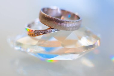 Refleksli iki nikah yüzüğünün yakın çekimi. Kristal bir taşın üzerinde.