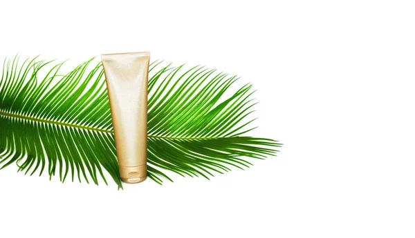 Gouden crème fles en tropisch blad op de witte achtergrond. — Stockfoto