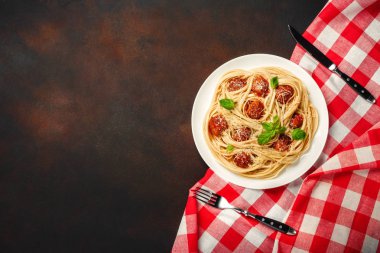 Spagetti makarna köfte ile kiraz ve domates sosu paslı arka planda, üstten görünüm.