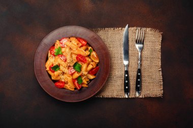 Makarna peynir, kiraz domates, çatal ve bıçak paslı arka planda, üstten görünüm.