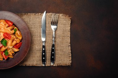 Makarna peynir, kiraz domates, çatal ve bıçak paslı arka planda, üstten görünüm.