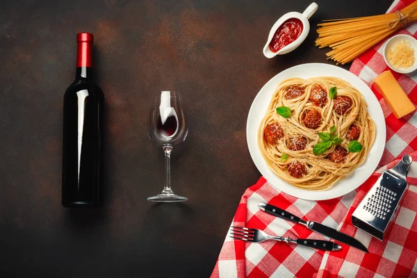 Spaghetti pasta with meatballs, cherry tomato sauce, wineglass and bottle on rusty background, top view.