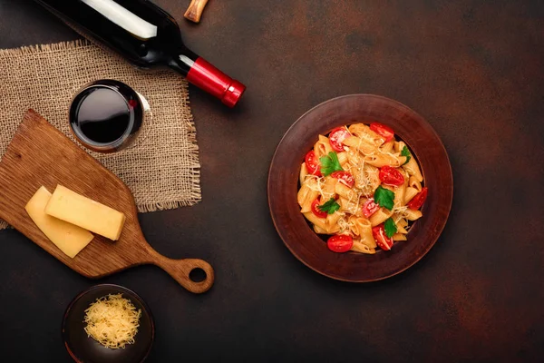 Pasta with cheese, cherry tomato sauce, wineglass and bottle wine on rusty background, top view.
