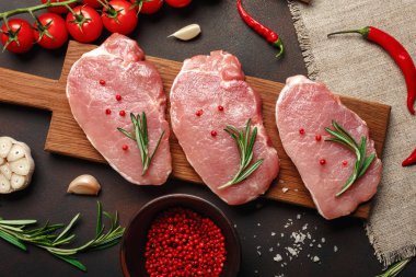 Çiğ domuz biftek domates, biberiye, sarımsak, biber, tuz ve baharat harç paslı kahverengi zemin üzerine ile kesme tahtası üzerinde parçaları. Üstten görünüm.