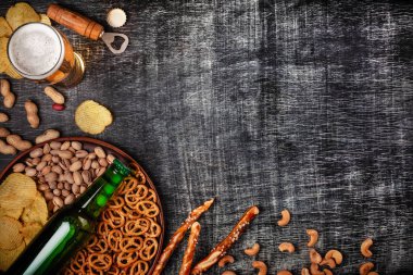 Bir şişe bira bir plaka ile tuzlu ookies simit, fıstık fındık ve cips siyah çizik tebeşir tahtası üzerinde. Üstten görünüm.