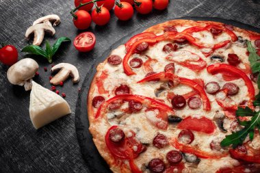 Pizza Tütsülenmiş sosis, peynir, mantar, domates, biber ve yeşillik bir taş ve bir siyah tebeşir tahtası, üstten görünüm.