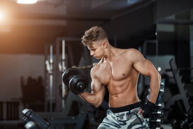 Spor salonunda ağırlık kaldıran kaslı bir delikanlının karanlık arka planda fotoğrafını çek..