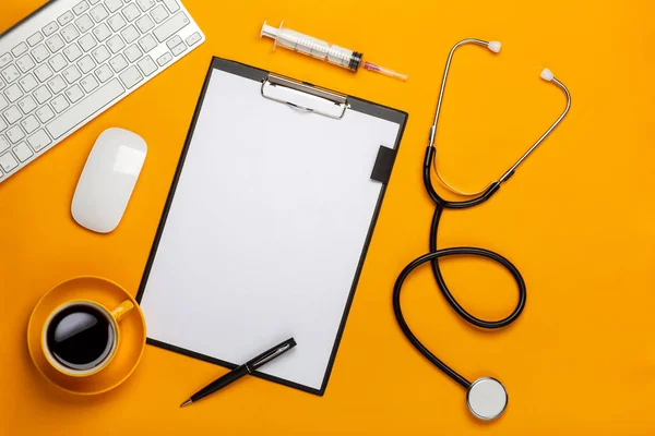 Tablonun bir doktorun not defteri ve kalem stetoskop, klavye, reçete ve ilaç, bir fincan kahve senin metin için yer ile sarı bir arka plan üzerinde üstten görünüm.