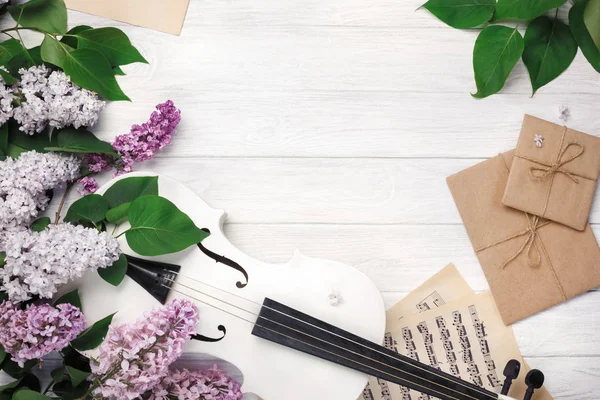 A bouquet of lilacs with violin, letter and music sheet on a white wooden table. Top wiev with space for your text.